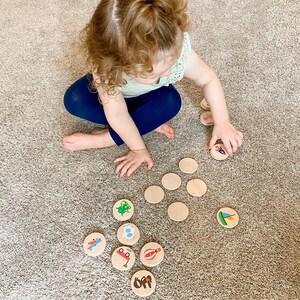 May include: A child is playing with wooden circle toys with colorful illustrations. The child is wearing a light green top and blue pants. The toys are scattered on a beige carpet.