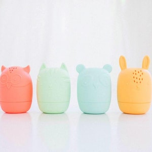 Puede incluir: Cuatro pequeños recipientes de silicona redondeados con forma de animales. De izquierda a derecha, las figuras son un búho coral, un gato verde claro, un oso azul pálido y un conejo amarillo. Cada recipiente tiene detalles faciales en relieve.