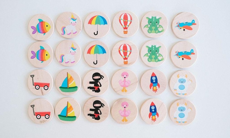 May include: Wooden circle game pieces with colorful illustrations of a rainbow fish, unicorn, umbrella, hot air balloon, dragon, airplane, wagon, sailboat, ninja, flamingo, rocket, and yeti. The game pieces are arranged on a white surface.
