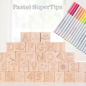 May include: Wooden alphabet blocks with etched letters, numbers, and illustrations, stacked in a pyramid. A set of pastel-colored markers is arranged diagonally in the background. The text "Pastel SuperTips" is at the top.
