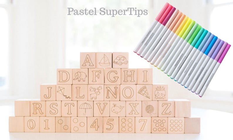 May include: Wooden alphabet blocks with etched letters, numbers, and illustrations, stacked in a pyramid. A set of pastel-colored markers is arranged diagonally in the background. The text "Pastel SuperTips" is at the top.