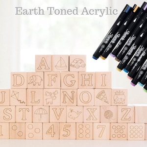 May include: Wooden alphabet blocks with etched letters and illustrations, stacked in a pyramid. The blocks are accompanied by a set of colorful Sharpie markers. The text "Earth Toned Acrylic" is at the top.