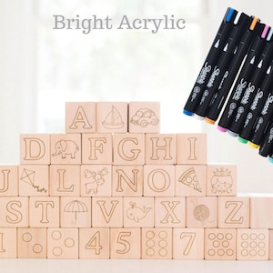 May include: Wooden alphabet blocks with engraved letters and illustrations, stacked in a pyramid. A set of Sharpie markers with various colored tips is displayed next to the blocks. The text "Bright Acrylic" is at the top.