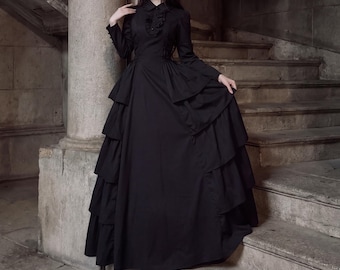 May include: A floor-length black dress featuring long sleeves, a collared neckline with vertical ruffles, and a multi-layered skirt with tiered panels. The bodice is fitted with a button-down front, and the skirt has a full, voluminous silhouette.