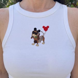May include: White ribbed tank top with an embroidered cartoon dachshund wearing sunglasses and a Mickey Mouse-shaped balloon. The dachshund has a brown body, a skeleton-like design, and is holding a red balloon.