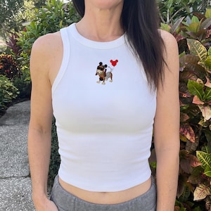 May include: White ribbed tank top with a cartoon dachshund wearing sunglasses and holding a red heart-shaped balloon. The dachshund is brown, gray, and tan. The tank top is sleeveless and has a round neckline.
