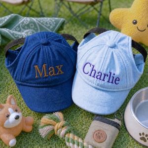 May include: Two baseball caps with ear holes, one dark blue with the name Max embroidered in gold and one light blue with the name Charlie embroidered in purple. Both caps feature a black adjustable strap and a structured six-panel design.