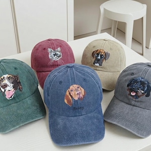 Può includere: Cinque cappellini da baseball in vari colori, tra cui verde, bordeaux, blu, beige e grigio. Ogni cappellino presenta un ritratto di animale ricamato sul pannello frontale. Il cappellino blu ha il nome Benny ricamato sotto il ritratto del cane.