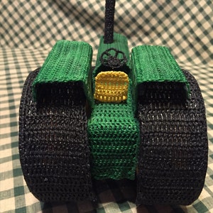 May include: A green and black crocheted toy tractor with large wheels. The tractor has a yellow crocheted detail on the front.