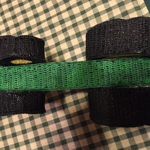 May include: A green crocheted band with black crocheted circles on either end. The circles are stacked on top of each other.