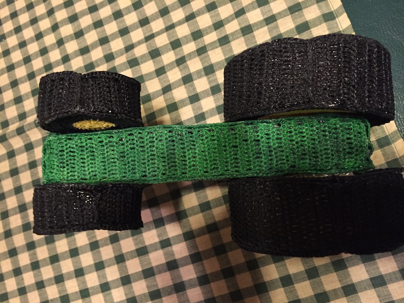 May include: A green crocheted band with black crocheted circles on either end. The circles are stacked on top of each other.
