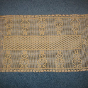 Puede incluir: Un camino de mesa de ganchillo beige con un patrón delicado. El camino de mesa presenta un diseño repetitivo de pequeños círculos y una banda central de círculos más pequeños.