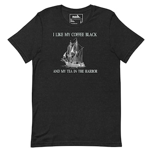 Può includere: T-shirt grigio scuro con la scritta "I LIKE MY COFFEE BLACK AND MY TEA IN THE HARBOR" e un'illustrazione bianca di una nave a vela. Un piccolo logo è visibile nella parte superiore della maglietta.