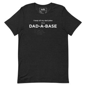 May include: Charcoal grey t-shirt featuring the white text "I keep all my dad jokes in a DAD-A-BASE". The shirt has a small logo at the top. A funny graphic tee, perfect for fans of dad jokes.