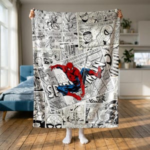 May include: A rectangular throw blanket featuring a black and white comic book print with various panels depicting Spider-Man. A large, central, full-colour illustration shows Spider-Man in a red and blue suit with the text The Amazing Spider-Man.