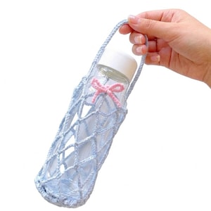 May include: A light blue crocheted water bottle holder with a pink bow. The holder is designed to carry a clear water bottle with a white cap. The handle is also crocheted. The bottle is held in place by the crocheted netting.