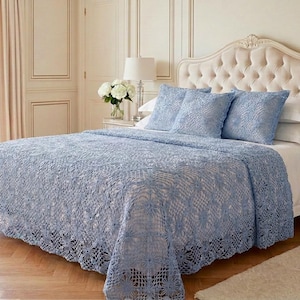May include: A light blue crochet bedspread and three matching square throw pillows featuring an intricate floral pattern. The bedding is draped over a white bed sheet set on a tufted cream-colored headboard, creating a layered textile display.