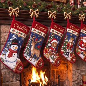 Könnte beinhalten: Sechs Weihnachtsstrümpfe hängen an goldenen Schleifenhaken. Jeder Strumpf hat einen roten Umschlag mit den eingestickten Namen: Cecilia, Sophia, David, Oliver, Althea und Esther. Die blauen Körper zeigen festliche Motive wie Schneemann, Hirsch, Teddybär, Nussknacker und Weihnachtsmann.