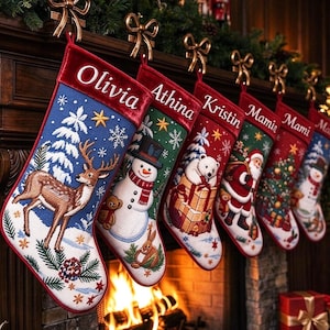 Op de afbeelding: Een rij van zes gepersonaliseerde kerstsokken hangend aan een schoorsteenmantel. Elke sok is voorzien van een unieke geborduurde kerstscène, waaronder een hert, sneeuwpop, ijsbeer en de Kerstman, met namen in wit geborduurd op rode fluwelen boorden.