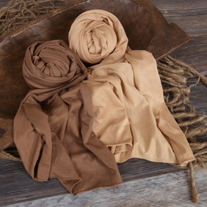 May include: Two fabric wraps in brown and beige tones, arranged on a wooden surface. The wraps are made of a soft, stretchy material and are perfect for newborn photography.
