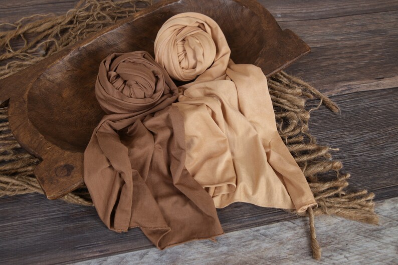 May include: Two fabric wraps in brown and beige tones, arranged on a wooden surface. The wraps are made of a soft, stretchy material and are perfect for newborn photography.