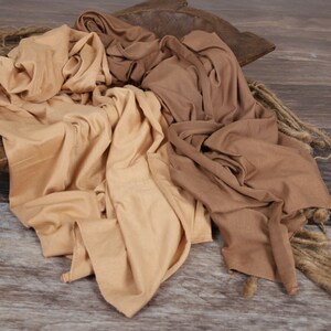 May include: Two fabric swaddles in beige and brown colors, arranged in a wooden bowl on a woodgrain background.