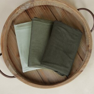 May include: Three fabric swatches in a wooden tray. The swatches are in shades of green and light green.