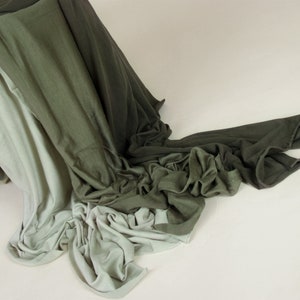 May include: A pile of fabric in shades of green and white. The fabric is draped over a wooden box and flows down onto a white surface.