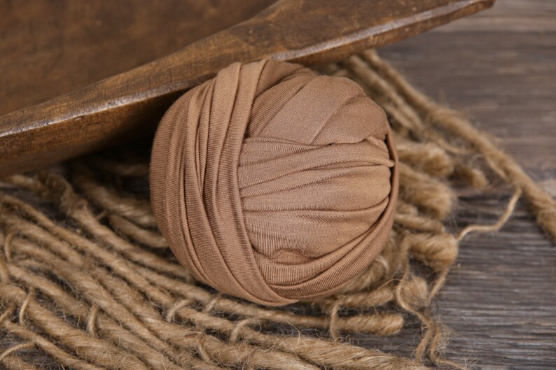 May include: A brown fabric roll for newborn photography. The roll is made of soft, stretchy fabric and is perfect for creating a variety of poses.