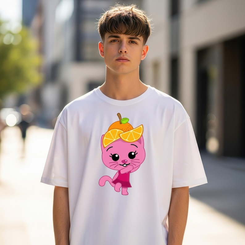 May include: White t-shirt featuring a cartoon pink cat wearing an orange hat with orange slices. The cat is smiling and wearing a pink dress. The shirt is a casual style.