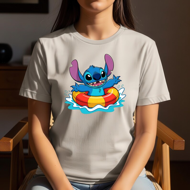 May include: A light beige t-shirt featuring a cartoon image of Stitch from Lilo & Stitch. Stitch, a blue alien, is in a red and yellow inflatable ring in blue water. The shirt is short-sleeved.