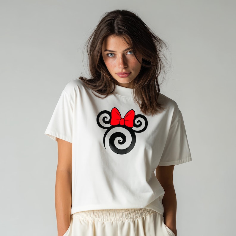 May include: A white short-sleeved t-shirt featuring a graphic print on the chest. The design consists of a black spiral-shaped silhouette resembling a mouse head, accented with a bright red bow positioned between the two circular ears.