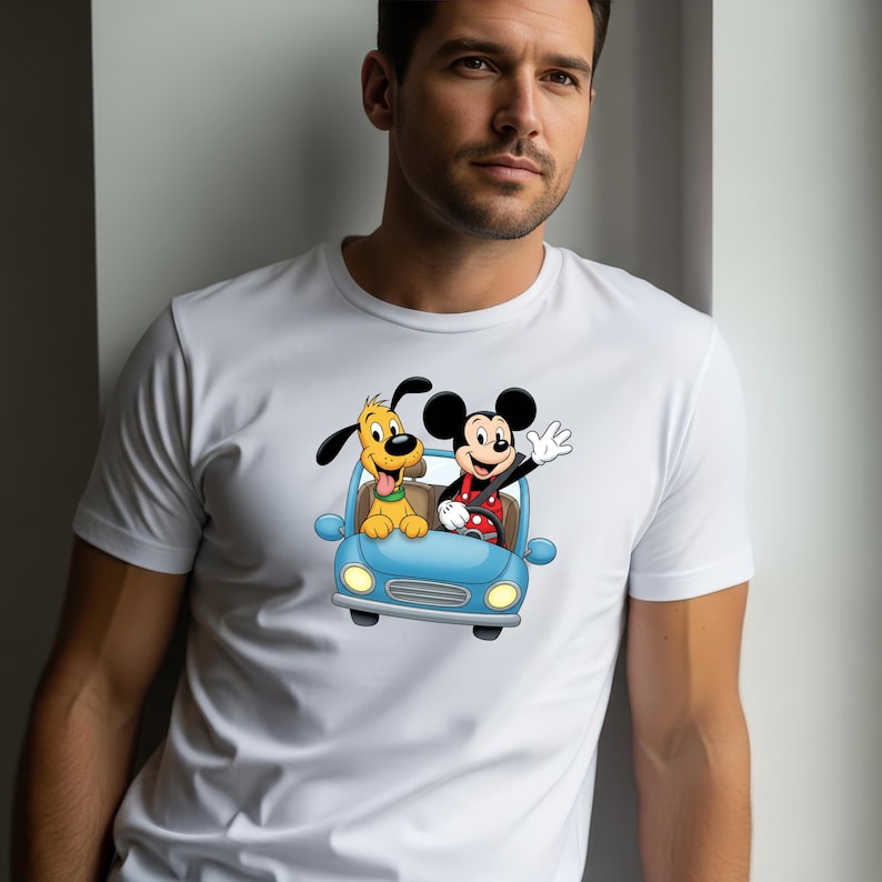 May include: A white short-sleeved crew neck t-shirt featuring a colorful graphic print of a cartoon mouse and a yellow dog riding together in a light blue car. The mouse is waving a hand while the dog has its tongue out in the passenger seat.