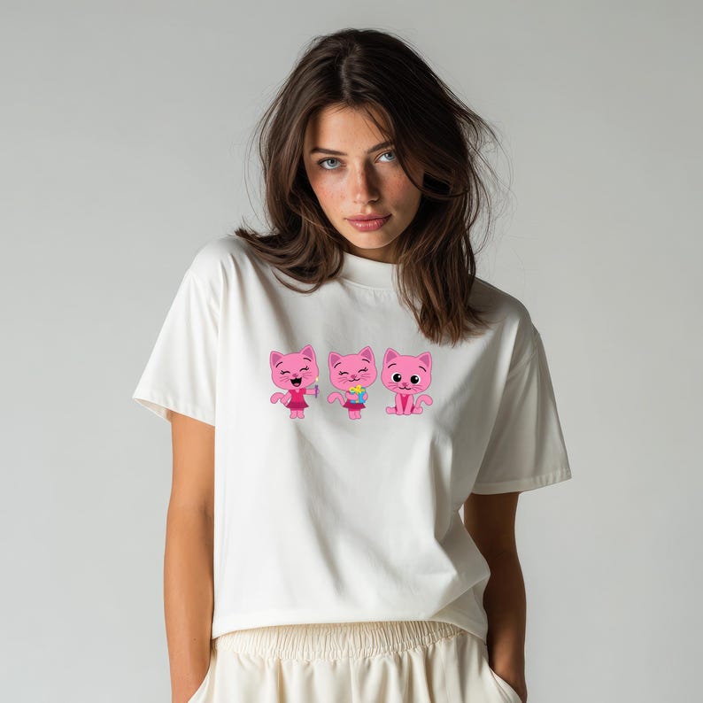 May include: A white t-shirt featuring three pink cartoon cat characters. The cats have different expressions and are wearing various accessories. The t-shirt is made of a soft, comfortable material.