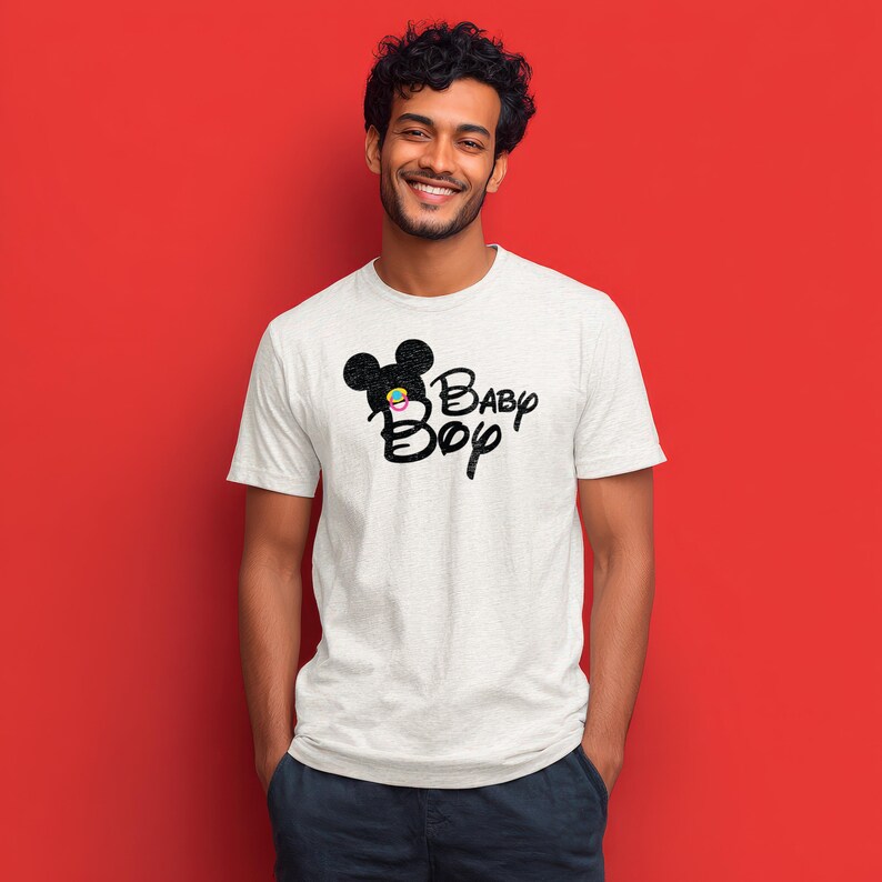 May include: A light gray short-sleeved t-shirt featuring a black graphic of a mouse silhouette with a small colorful pacifier in the center, accompanied by the black text Baby Boy written in a stylized script font across the chest area.