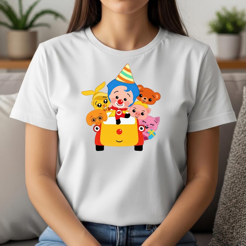 May include: White t-shirt featuring a colorful cartoon design. The graphic shows a clown driving a yellow car with various animal characters. The clown wears a party hat, and the car has red accents. A fun and playful design.