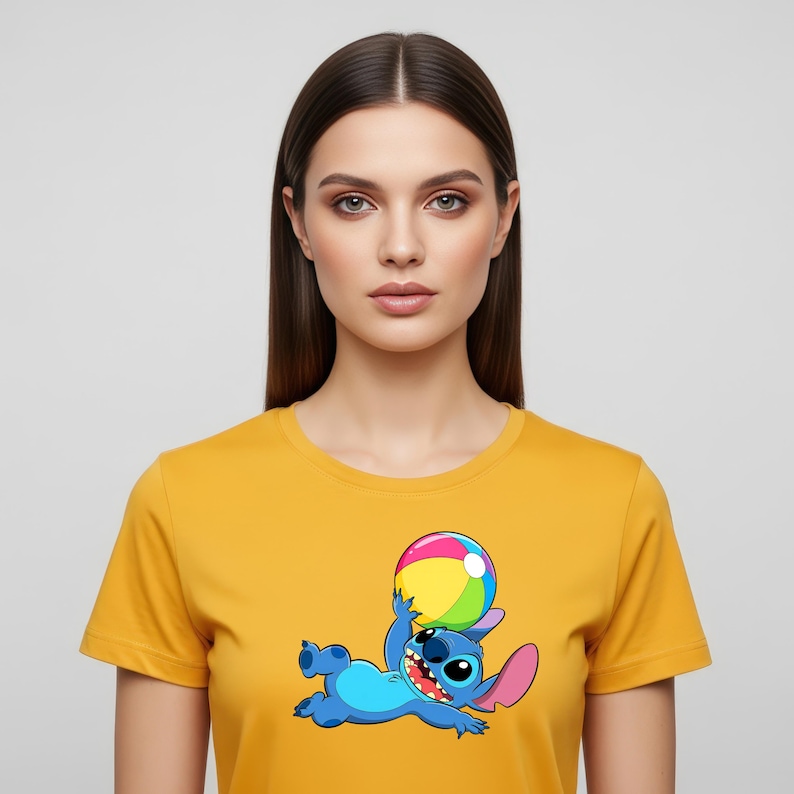 May include: Mustard yellow t-shirt featuring a cartoon graphic of the character Stitch from Lilo & Stitch. Stitch is blue with large ears and is holding a colorful beach ball. The shirt has short sleeves and a crew neck.