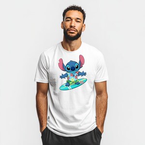May include: White t-shirt featuring a cartoon illustration of Stitch surfing on a blue surfboard. Stitch is blue with large ears, wearing a Hawaiian shirt with floral patterns and green shorts. The shirt is worn by a person.