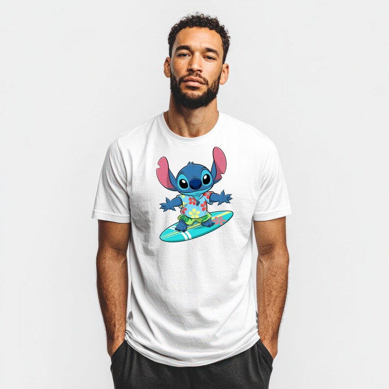 May include: White t-shirt featuring a cartoon illustration of Stitch surfing on a blue surfboard. Stitch is blue with large ears, wearing a Hawaiian shirt with floral patterns and green shorts. The shirt is worn by a person.