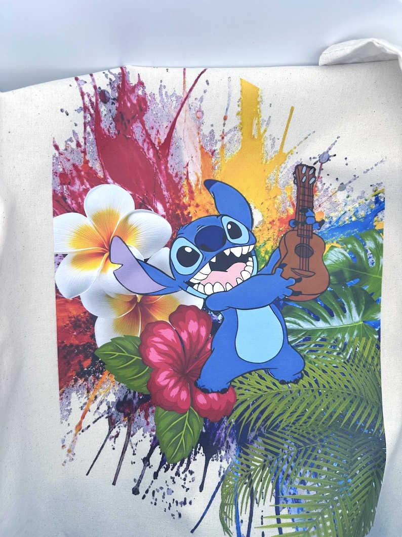 May include: Cream tote bag with a blue cartoon character holding a ukulele. The design includes vibrant paint splashes, tropical flowers, and palm leaves. The character has large eyes and a wide grin.
