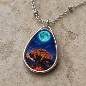 May include: A silver-toned teardrop-shaped pendant necklace featuring a graphic print of an orange jumping spider perched on a branch under a bright teal full moon in a desert landscape at twilight, suspended from a delicate silver chain.