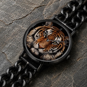 K&ouml;nnte beinhalten: Eine runde Armbanduhr mit einem detaillierten Tigergesicht auf dem Zifferblatt, eingefasst in ein schwarzes Metallgeh&auml;use. Die Uhr verf&uuml;gt &uuml;ber ein schwarzes Metallgliederarmband und d&uuml;nne schwarze Zeiger in einem kontrastreichen Design.
