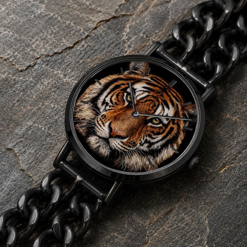 K&ouml;nnte beinhalten: Eine runde Armbanduhr mit einem detaillierten Tigergesicht auf dem Zifferblatt, eingefasst in ein schwarzes Metallgeh&auml;use. Die Uhr verf&uuml;gt &uuml;ber ein schwarzes Metallgliederarmband und d&uuml;nne schwarze Zeiger in einem kontrastreichen Design.