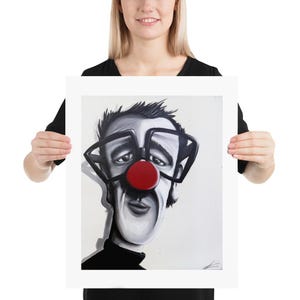 Peut inclure: Une caricature en noir et blanc d'un homme avec un nez de clown rouge et de grandes lunettes carrées. L'homme porte un col roulé noir. L'œuvre est affichée sur un fond blanc.