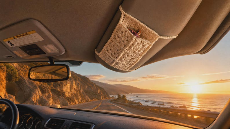 May include: A cream-colored, crocheted fabric organizer sleeve attached to a car sun visor. The sleeve features a textured, grid-like pattern and is designed to hold small items securely against the visor, visible inside a vehicle interior.