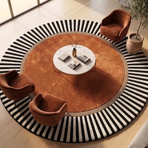 May include: A large circular area rug featuring a solid burnt orange center surrounded by a wide border of alternating black and white radial stripes. Three burnt orange upholstered armchairs are arranged around a white marble coffee table.
