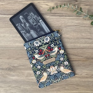 May include: A fabric e-reader sleeve featuring a dark blue background with a repeating pattern of birds, strawberries, and white flowers. A gold zip closure is at the top, and a small rectangular tag labelled HANDMADE is attached to the front.