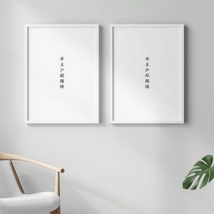 Peut inclure: Deux impressions d'art blanches encadrées avec des caractères japonais noirs sont accrochées à un mur gris clair. Une chaise en bois avec un coussin blanc est en dessous. Une plante en pot avec de grandes feuilles vertes est à droite.