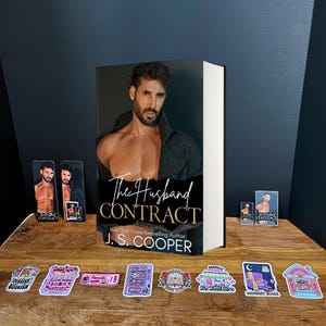 May include: A book titled "The Husband Contract" by J.S. Cooper, with a shirtless man on the cover. The image includes stickers with book-related designs and small promotional cards featuring the book cover.