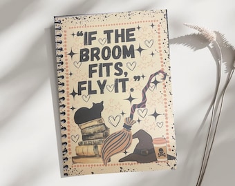May include: Spiral-bound notebook with a vintage-style design. The cover features the phrase "IF THE BROOM FITS, FLY IT" in black lettering, along with illustrations of a black cat, books, a witch's hat, and a broom. The background is beige with star and heart accents.